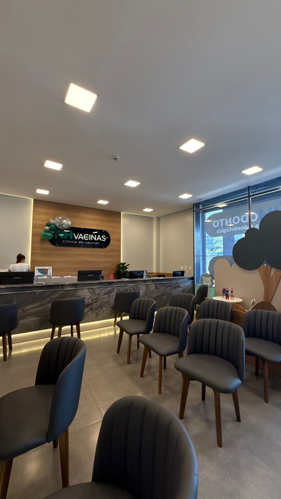 Recepção da NH Vacinas com logo, cadeiras cinza e área infantil ao fundo